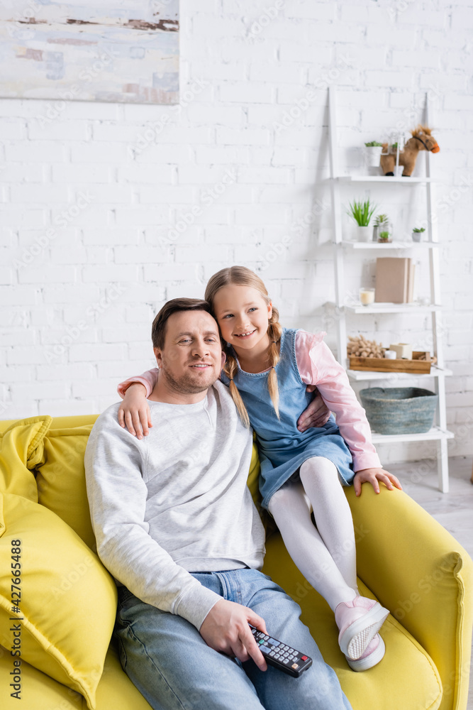 smiling child embracing father while watching movie on sofa at home smiling child embracing father while watching movie on sofa at home