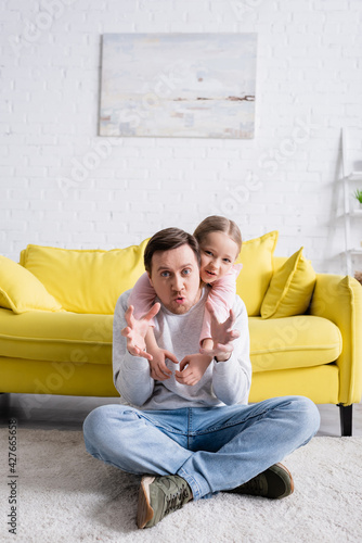Obraz na plátně man sitting on floor and showing frightening gesture near cheerful daughter