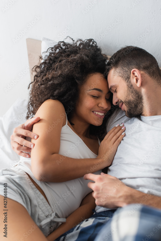 high angle view of cheerful interracial man and woman hugging while lying in bed high angle view of cheerful interracial man and woman hugging while lying in bed