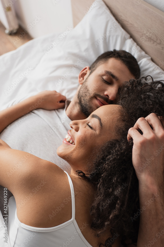 high angle view of cheerful interracial couple lying in bed at home high angle view of cheerful interracial couple lying in bed at home