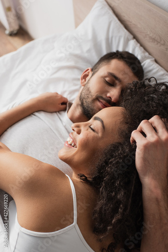 high angle view of cheerful interracial couple lying in bed at home
