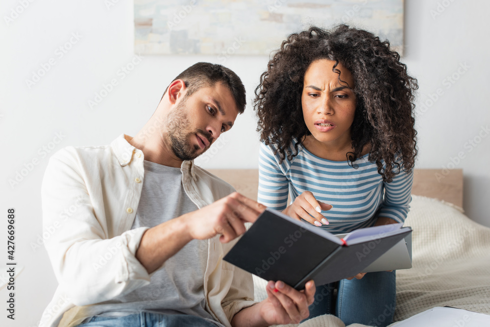 interracial couple looking at notebook in bedroom
