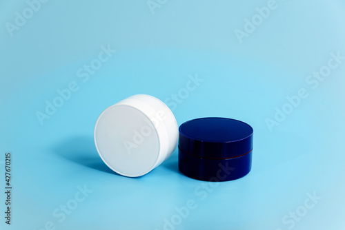 Obraz na płótnie Two closed plastic cream jars on light blue background. Blank white and blue cosmetic containers. Day and night facial care concept. Branding of beauty products. Mockup. Copy space. w salonie