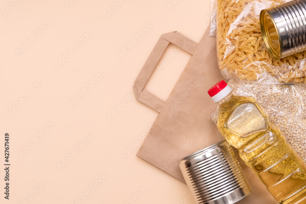 Paper bag with food supplies crisis food supply on a light yellow background, copy space. Pearl barley, pasta, canned food, sunflower oil. Food delivery, Donation, coronavirus
