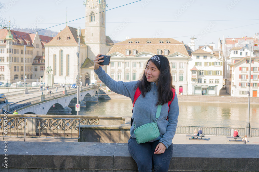Asian woman backpacker touring in Europe - young happy and pretty Korean girl with student backpack taking selfie with mobile phone during holidays in Europe