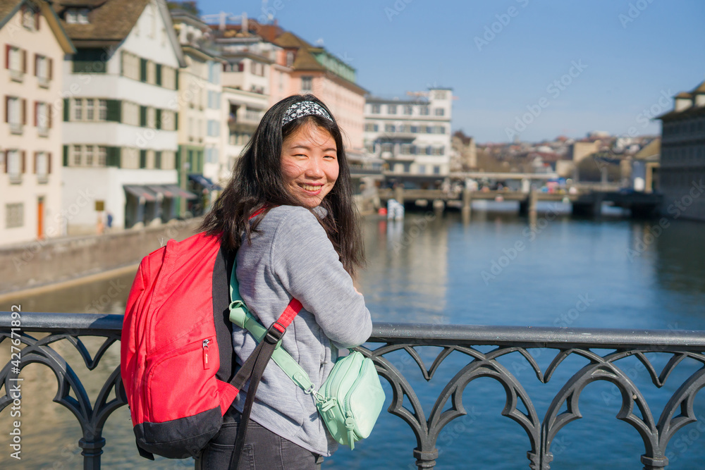 Asian woman backpacker touring in Europe - young happy and pretty Chinese girl with backpack having city and river view from bridge during holidays in Europe