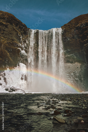 Waterfall Sk  gafoss with a bright rainbow in Iceland  vertical photo with no tourists. 