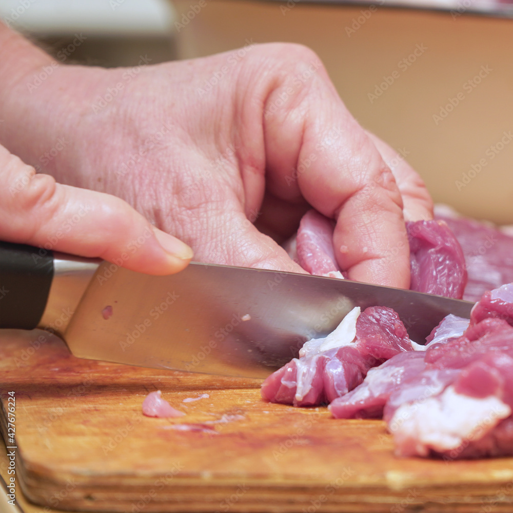 A woman cuts meat into pieces on a wooden chopping board