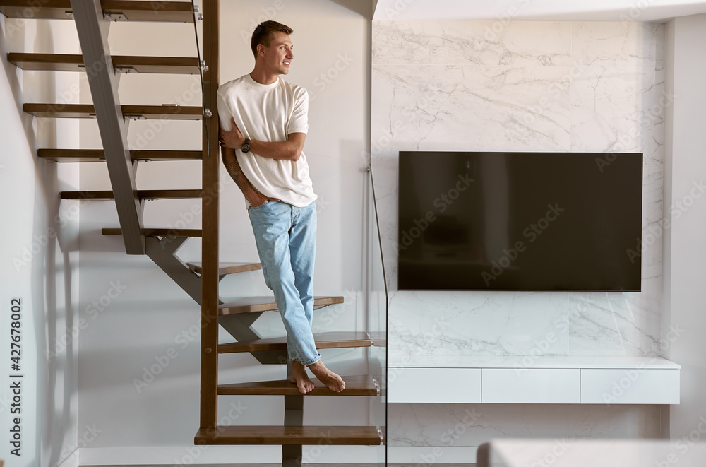 Relaxing happy caucasian man on the minimalistic stairs in modern light apartment