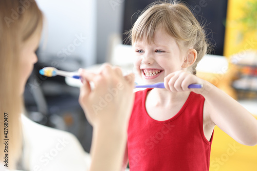 Little girl is taught how to properly brush her teeth with toothbrush