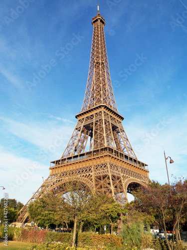 A beautiful view of the eiffel tower in summer among green trees against a blue bright sky