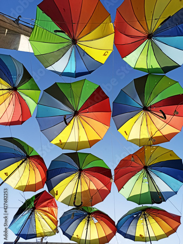 many hanging bright rainbow multi-colored umbrellas against the sky  bottom view