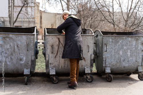 Fotografi homeless young guy rummages in trash cans in the park
