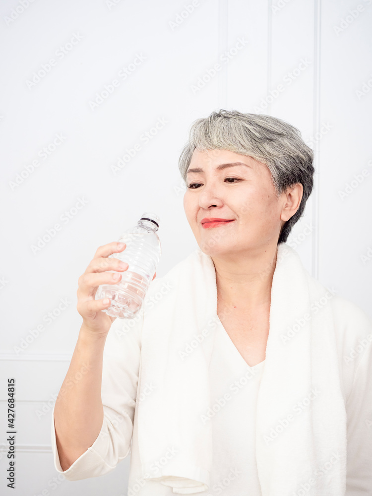 Senior asian woman taking a break while exercising at home. Athletic mature woman holding bottle of water. Senior asian woman taking a break while exercising at home. Athletic mature woman holding bottle of water.