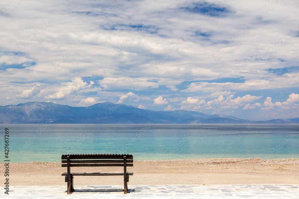Empty wooden bench by the sea in a cloudy day, gazing the Corinthian gulf, near Xylokastro town, in Peloponnese, Greece.