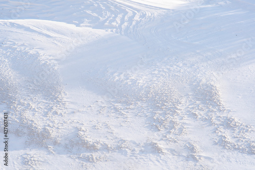 Top view of the snow-covered hill in the tundra. Snow with mud and long shadows