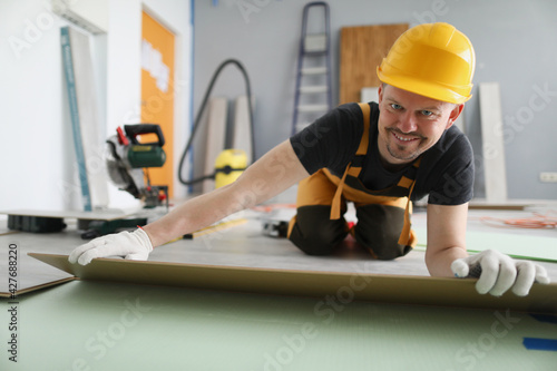 Man builder in yellow helmet lying laminate boards on floor