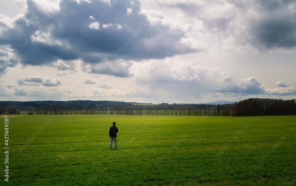 Young caucasian man walking, standing on meadow with dramatic sky. Czech spring landscape Young caucasian man walking, standing on meadow with dramatic sky. Czech spring landscape
