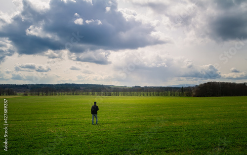 Young caucasian man walking, standing on meadow with dramatic sky. Czech spring landscape