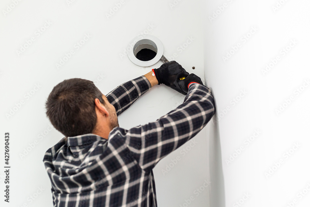 Naklejka premium Handyman with his tool removes the cover from the ventilation opening in the wall.