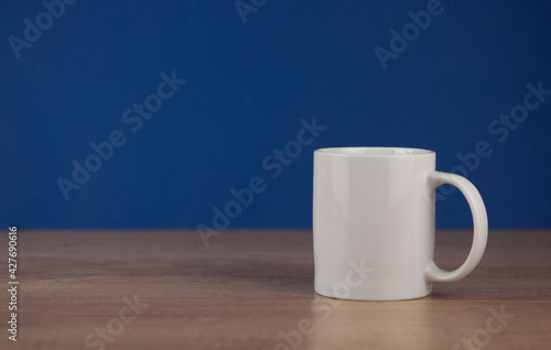 Single white cup on table against blue wall background