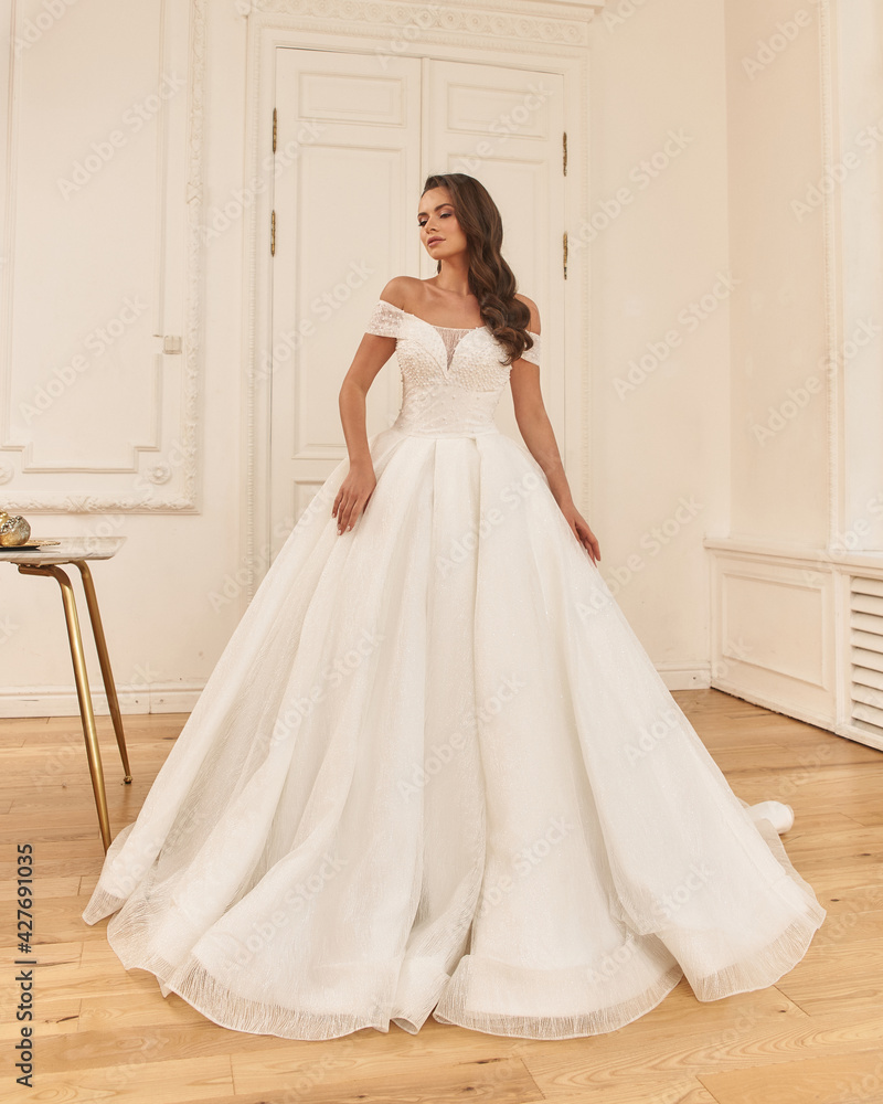 Elegant caucasian woman with natural make-up and hairstyle wearing white bridel dress, standing and posing in bright stylish interior. Full length portrait Elegant caucasian woman with natural make-up and hairstyle wearing white bridel dress, standing and posing in bright stylish interior. Full length portrait