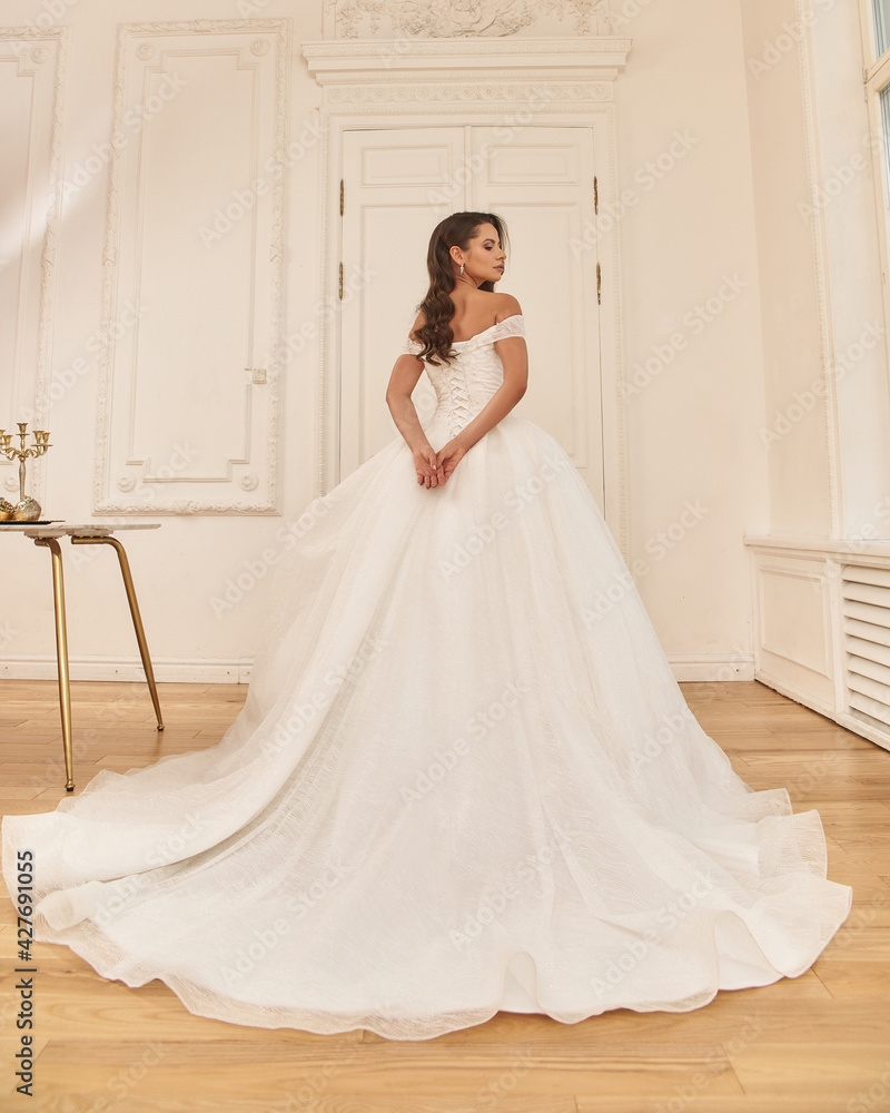 Elegant caucasian woman with natural make-up and hairstyle wearing white bridel dress, standing and posing in bright stylish interior. Full length portrait Elegant caucasian woman with natural make-up and hairstyle wearing white bridel dress, standing and posing in bright stylish interior. Full length portrait