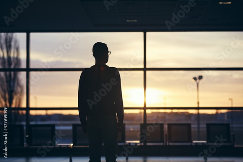 Pensive passenger waiting for airplane. Silhouette of man at airport at sunrise.