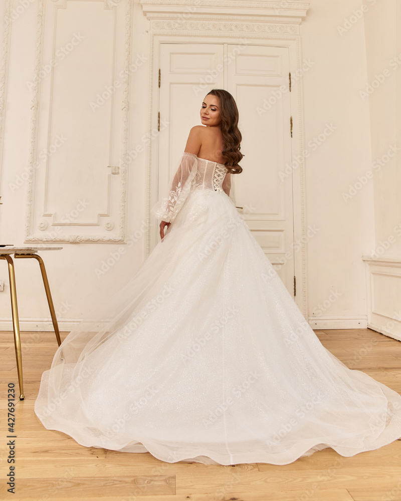 Elegant caucasian woman with natural make-up and hairstyle wearing white bridel dress, standing and posing in bright stylish interior. Full length portrait Elegant caucasian woman with natural make-up and hairstyle wearing white bridel dress, standing and posing in bright stylish interior. Full length portrait