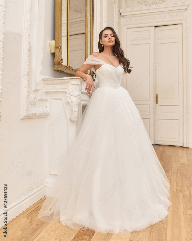 Portrait of young beautiful pretty elegant caucasian woman in white fluffy brifal dress standing in bright stylish interior and posing Portrait of young beautiful pretty elegant caucasian woman in white fluffy brifal dress standing in bright stylish interior and posing