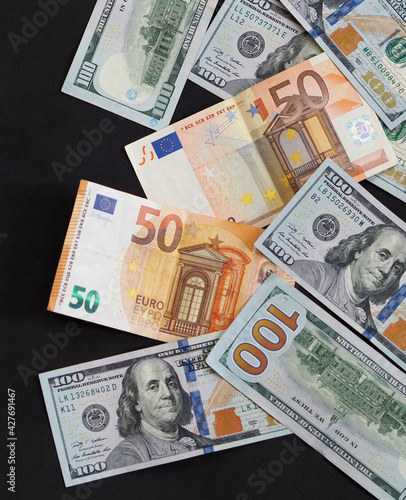 50 euro and 100 usd banknotes are standing side by side on a black background,