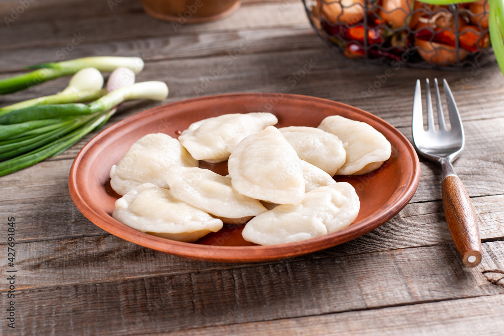 Dumplings, filled with mashed potato in plate on wooden table. Varenyky, vareniki, pierogi, pyrohy - dumplings with filling. Vegetarian dish. Dumplings, filled with mashed potato in plate on wooden table. Varenyky, vareniki, pierogi, pyrohy - dumplings with filling. Vegetarian dish.
