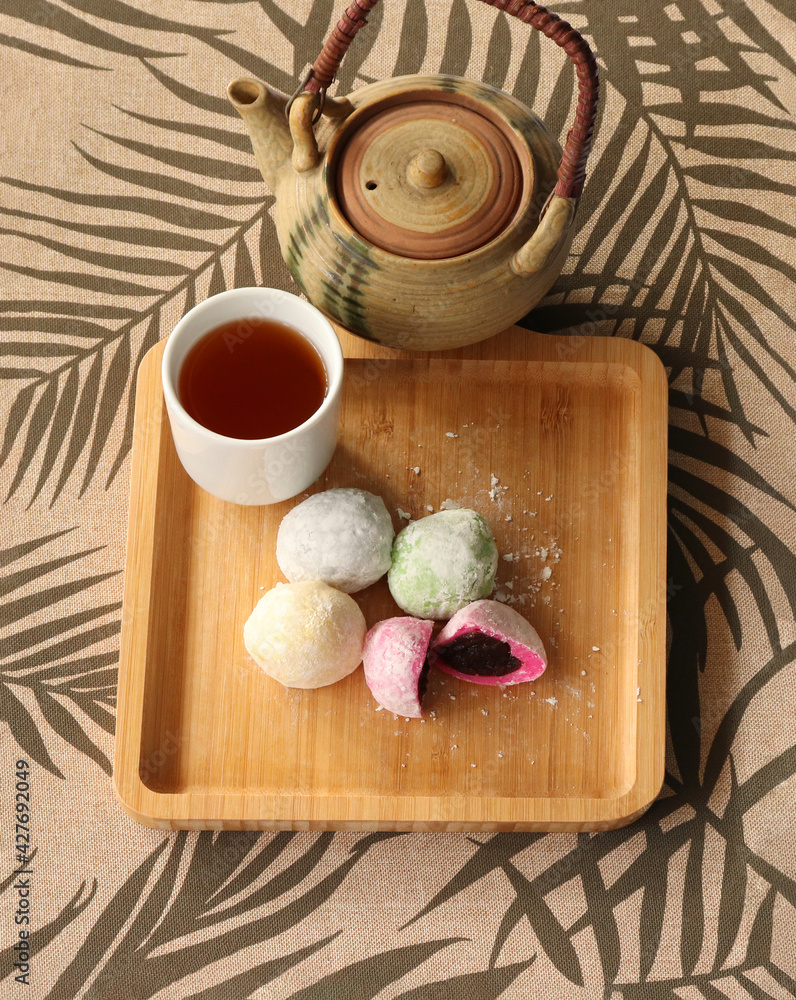 Daifuku Mochi stuffed with sweet red bean paste filling and put on the wooden tray, and Green tea. A teapot placed nearby. It is a traditional Japanese confectionery. Daifuku Mochi stuffed with sweet red bean paste filling and put on the wooden tray, and Green tea. A teapot placed nearby. It is a traditional Japanese confectionery.