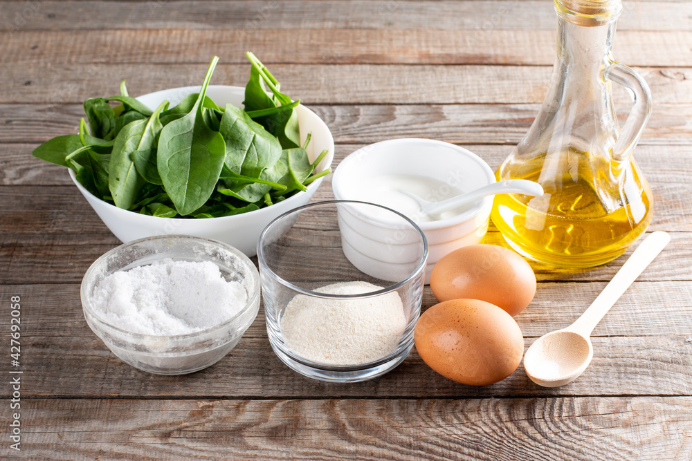 Set of raw ingredients for cooking healthy spinach pancakes on table (dough, psyllium, eggs, oil, sour cream and spinach leaves) Gluten free spinach pancakes recipe Set of raw ingredients for cooking healthy spinach pancakes on table (dough, psyllium, eggs, oil, sour cream and spinach leaves) Gluten free spinach pancakes recipe