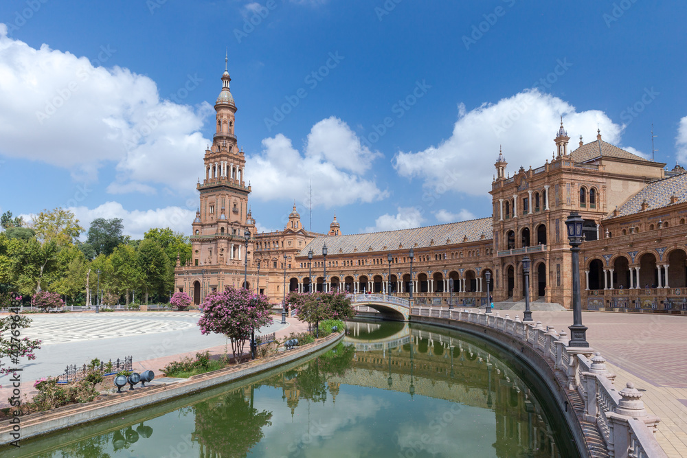 Spanish Square, in the center of Seville. Very touristic travel destination empty due to coronavirus measures. View of the south tower. Coloured flowers, blue  sky with few clouds. 