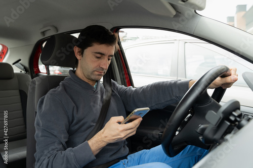 Young man driving car looking at cellphone on hand. Driver reckless behavior concept © Josu Ozkaritz