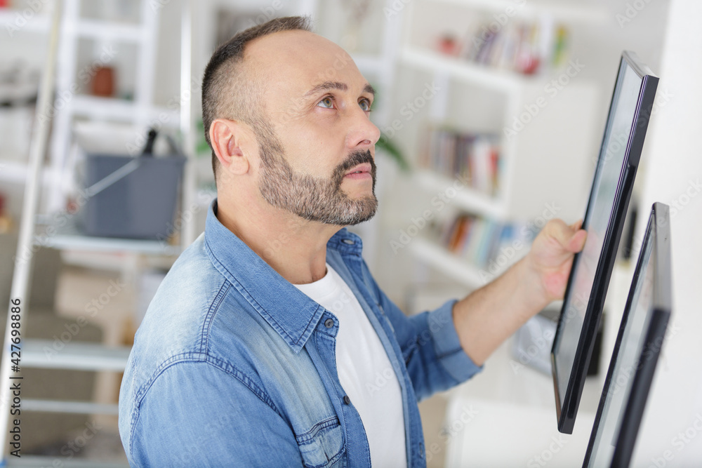 Fototapeta premium man hanging picture frames in his home
