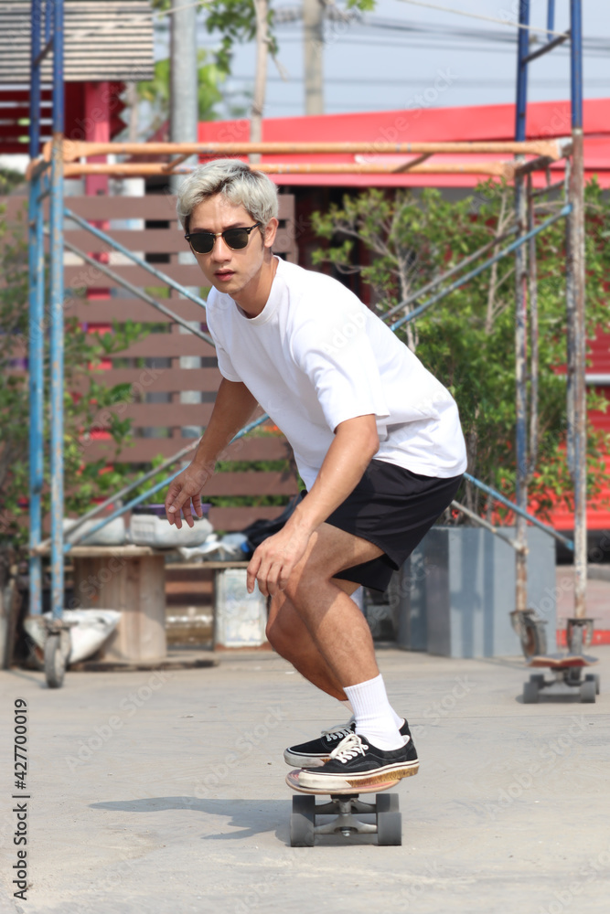 Young Asian man wearing sunglasses and playing surf skate board on the road outside on sunny day, man enjoy having fun with skateboard extreme sport activity outdoor.