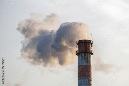 Smoke emission from the factory chimney against the blue sky background at evening