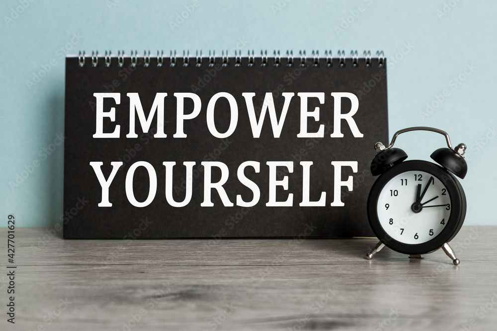 A word EMPOWER YOURSELF on black notebook with clock. Concept for time management and business. A word EMPOWER YOURSELF on black notebook with clock. Concept for time management and business.