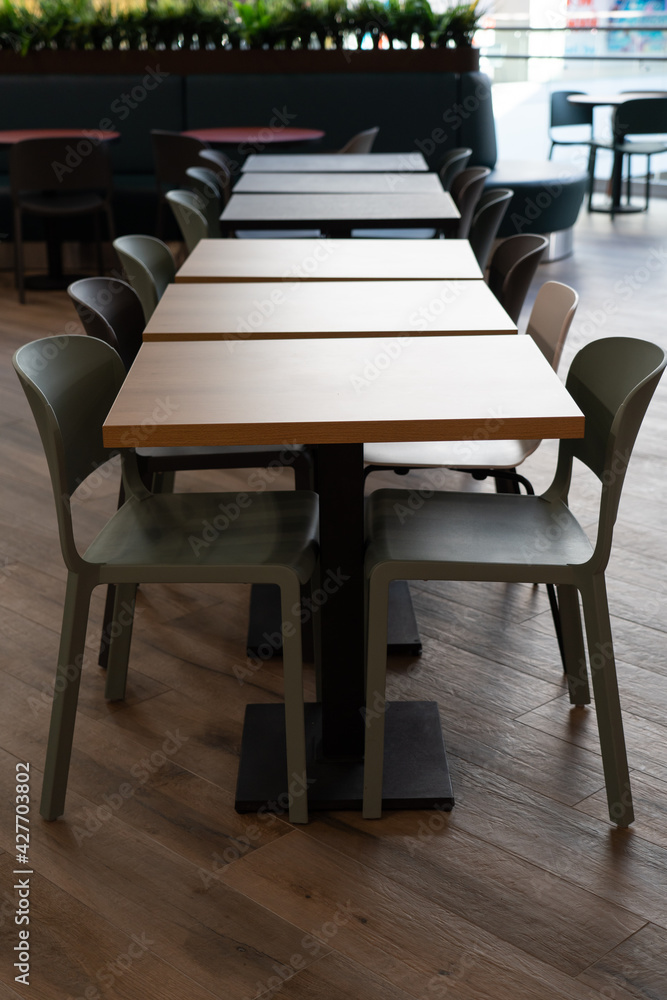 A row of tables with white chairs for visitors to the food court of a modern shopping center.