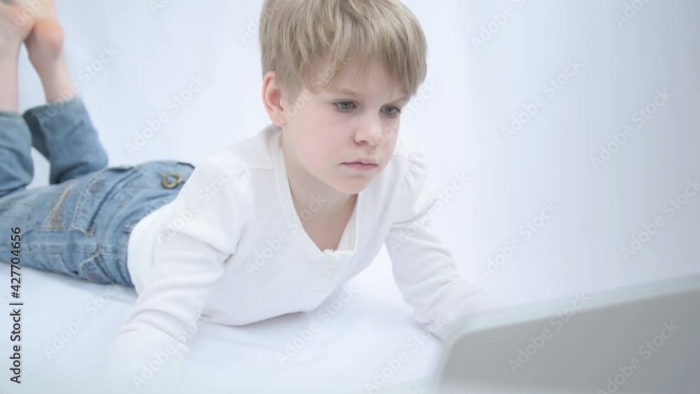 The blond child looks attentively at the computer or laptop screen. Close-up portrait The blond child looks attentively at the computer or laptop screen. Close-up portrait