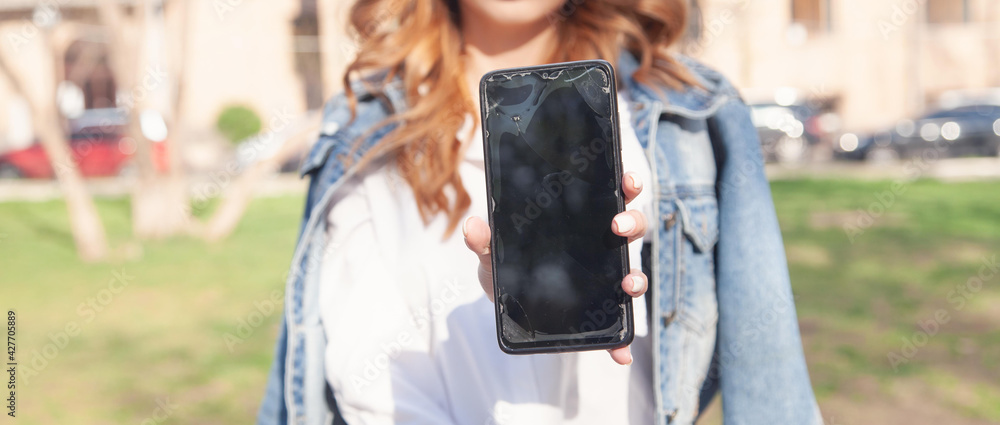 Young woman holding broken smartphone in outdoors.