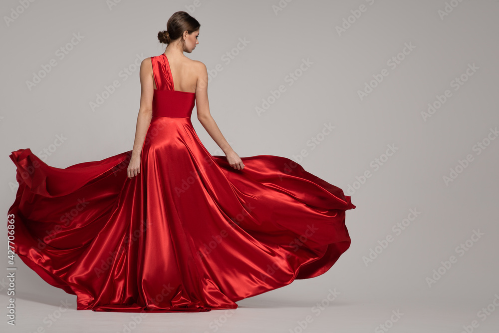 Fashion woman in red long dress on gray background. Back view - obrazy, fototapety, plakaty 