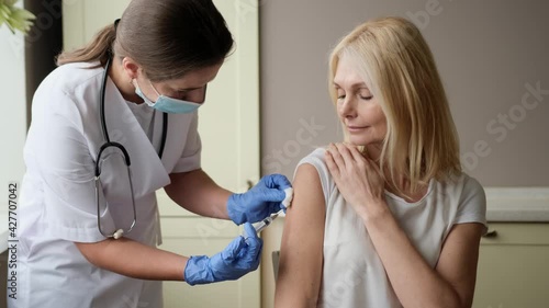 Professional doctor or nurse giving flu or COVID-19 injection to patient. Woman in medical face mask getting antiviral vaccine at hospital or health center during vaccination and immunization campaign