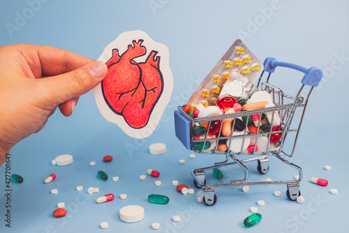 Treatment or prevention of heart diseases with variety of pills. pencil draw of human heart in hand against background of many colorful pills in grocery cart. Blue background.