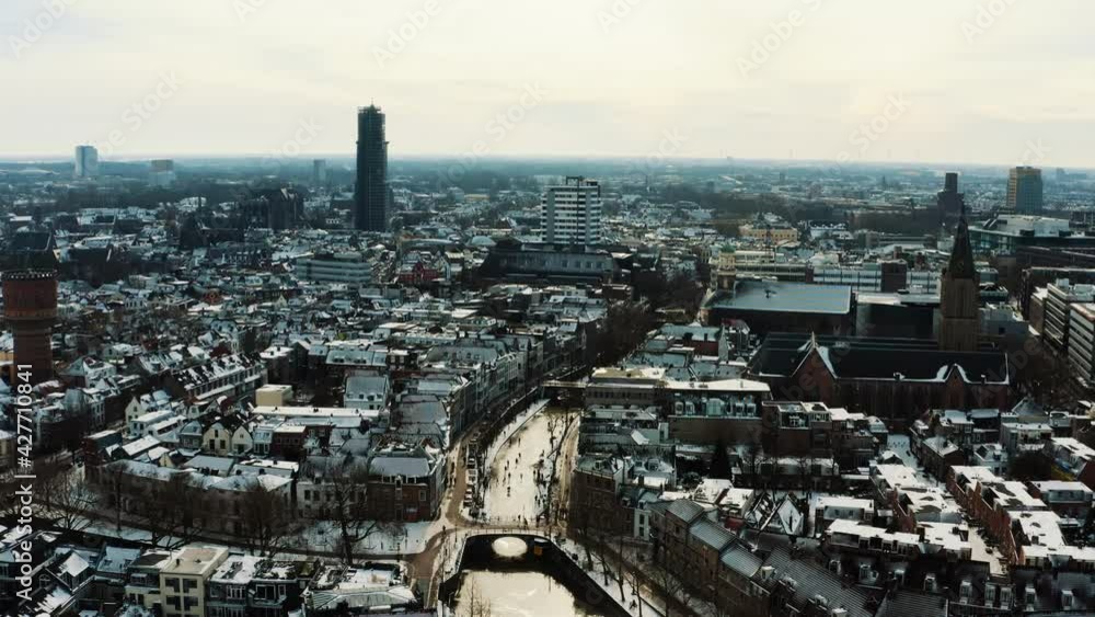 Aerial view, Utrecht, Netherlands on cold winter day, snow capped buildings and people ice skating on frozen canal water, drone shot Aerial view, Utrecht, Netherlands on cold winter day, snow capped buildings and people ice skating on frozen canal water, drone shot