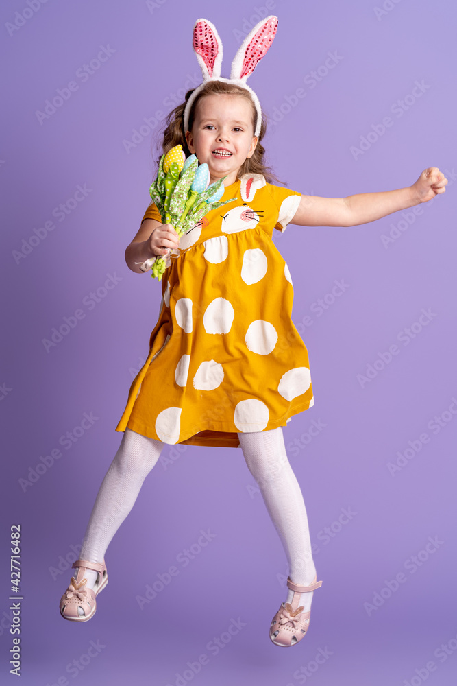 charming happy little girl with Easter bunny ears and a bouquet of spring tulip flowers made of fabric, jumping on a purple background. child smiles and rejoices at the arrival of spring and Easter