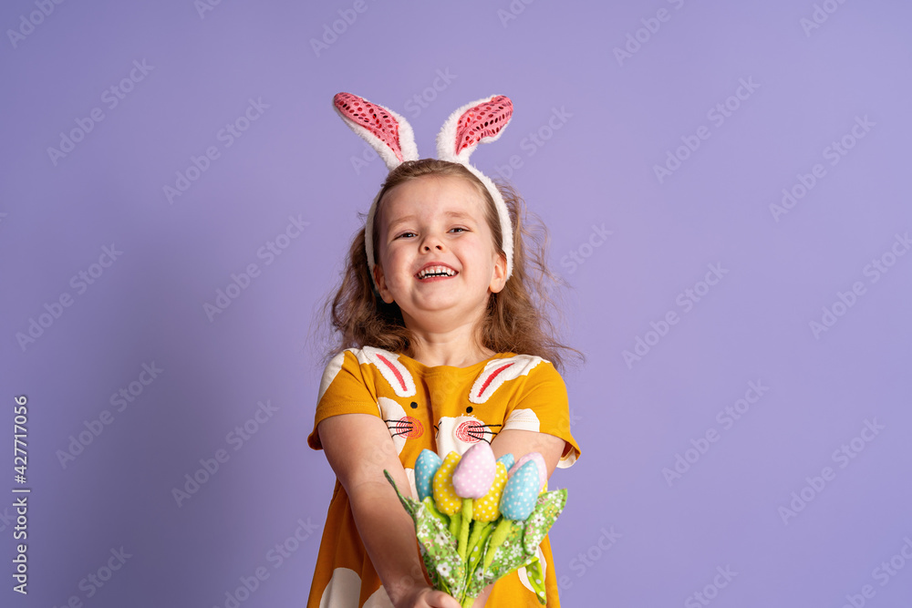 charming happy little girl with Easter bunny ears and a bouquet spring tulip flowers made fabric on purple background up to her waist. the child smiles and rejoices at the arrival of spring and Easter