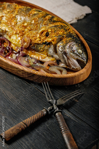 Close-up wooden dish with grilled fish. Sea food with vegetables on a dark wooden table. Sea trout. Delicious and healthy lunch or dinner. Mediterranean Kitchen. Vertical food photography photo